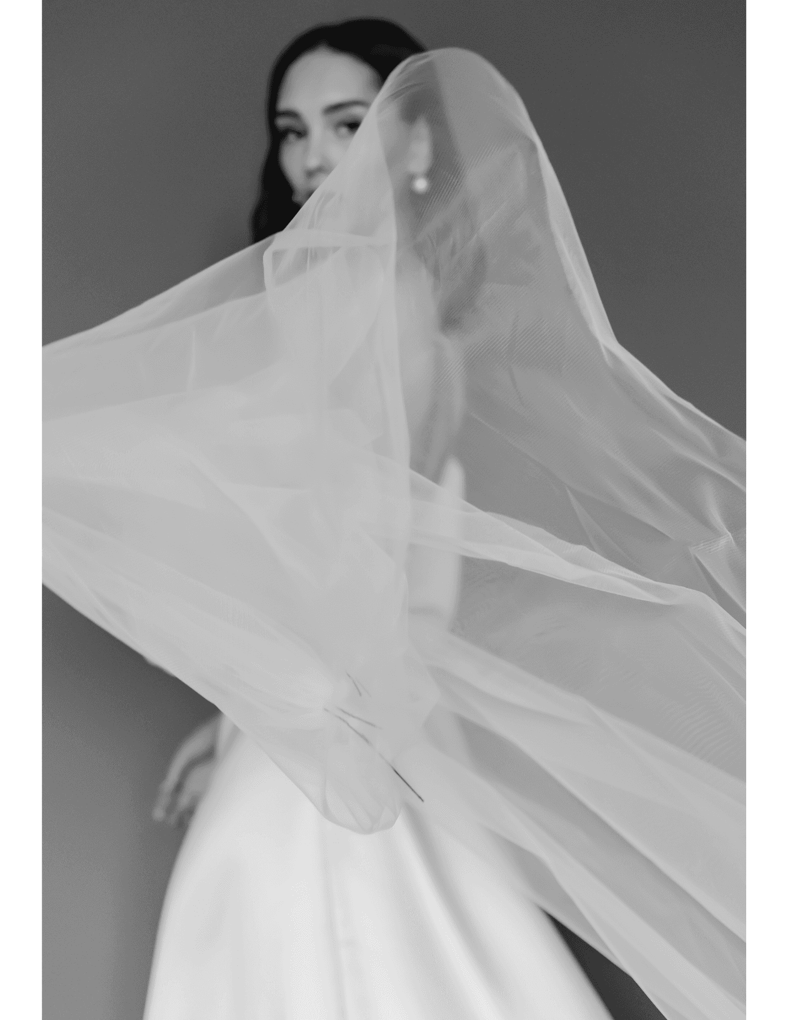 Bride posing, holding a flowing veil gracefully in black-and-white photograph.