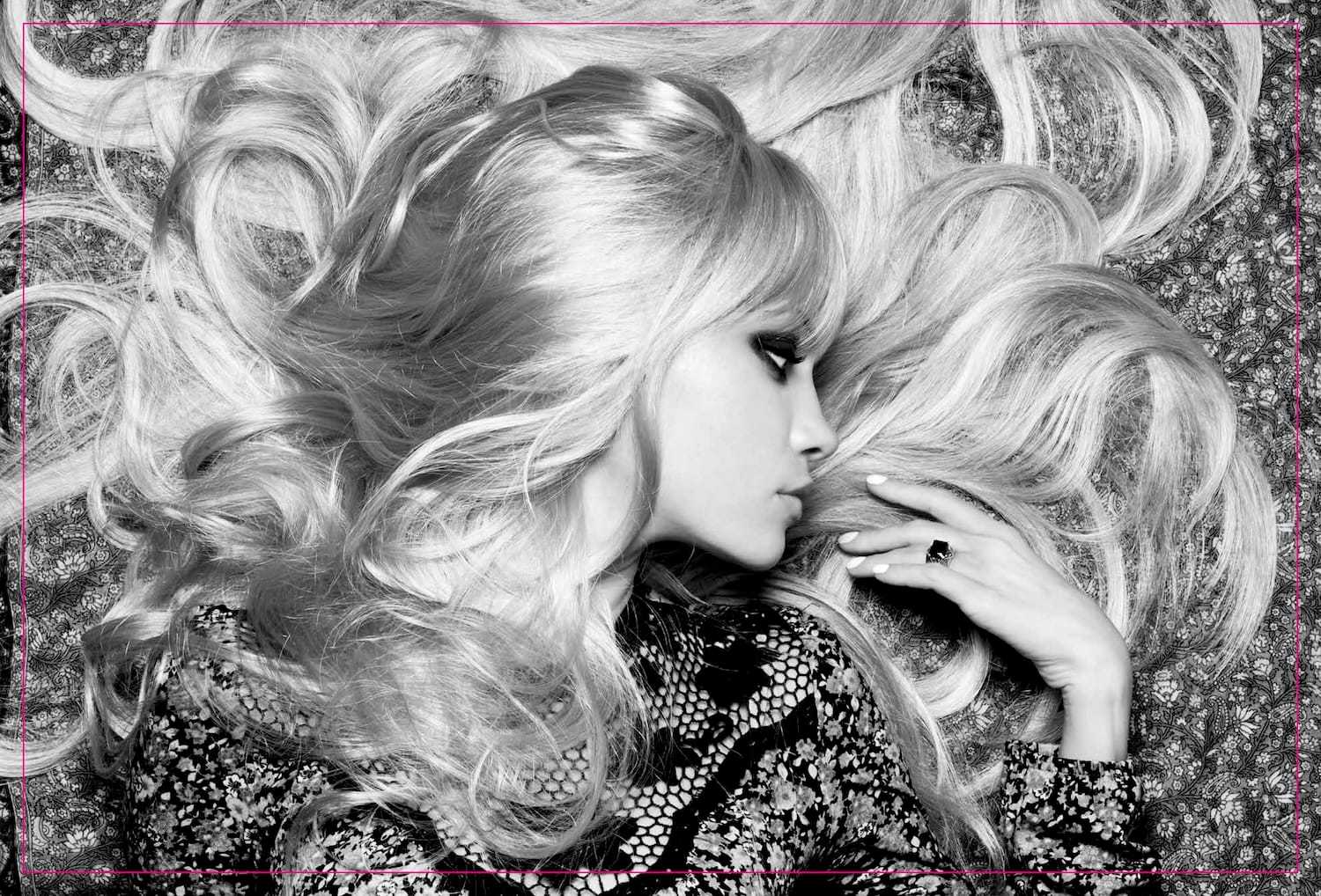 Blonde woman with voluminous hair lying on patterned backdrop.